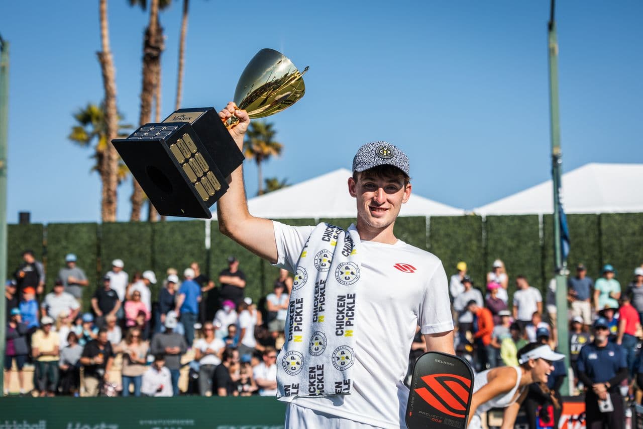 Dylan Frazier raising a championship trophy on a sunlit pickleball court