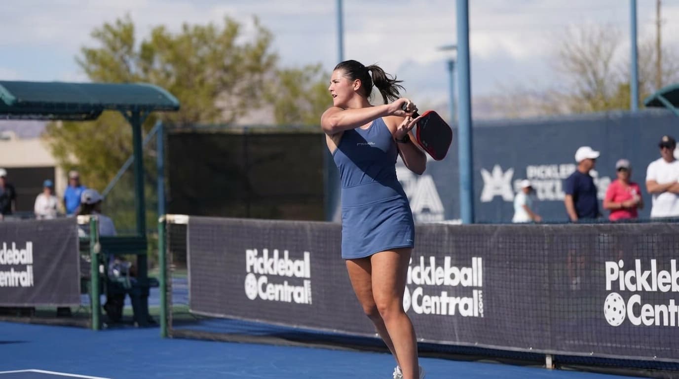 Zoey Weil following through on a two-handed backhand in a blue dress, Pickleball Central tournament backdrop