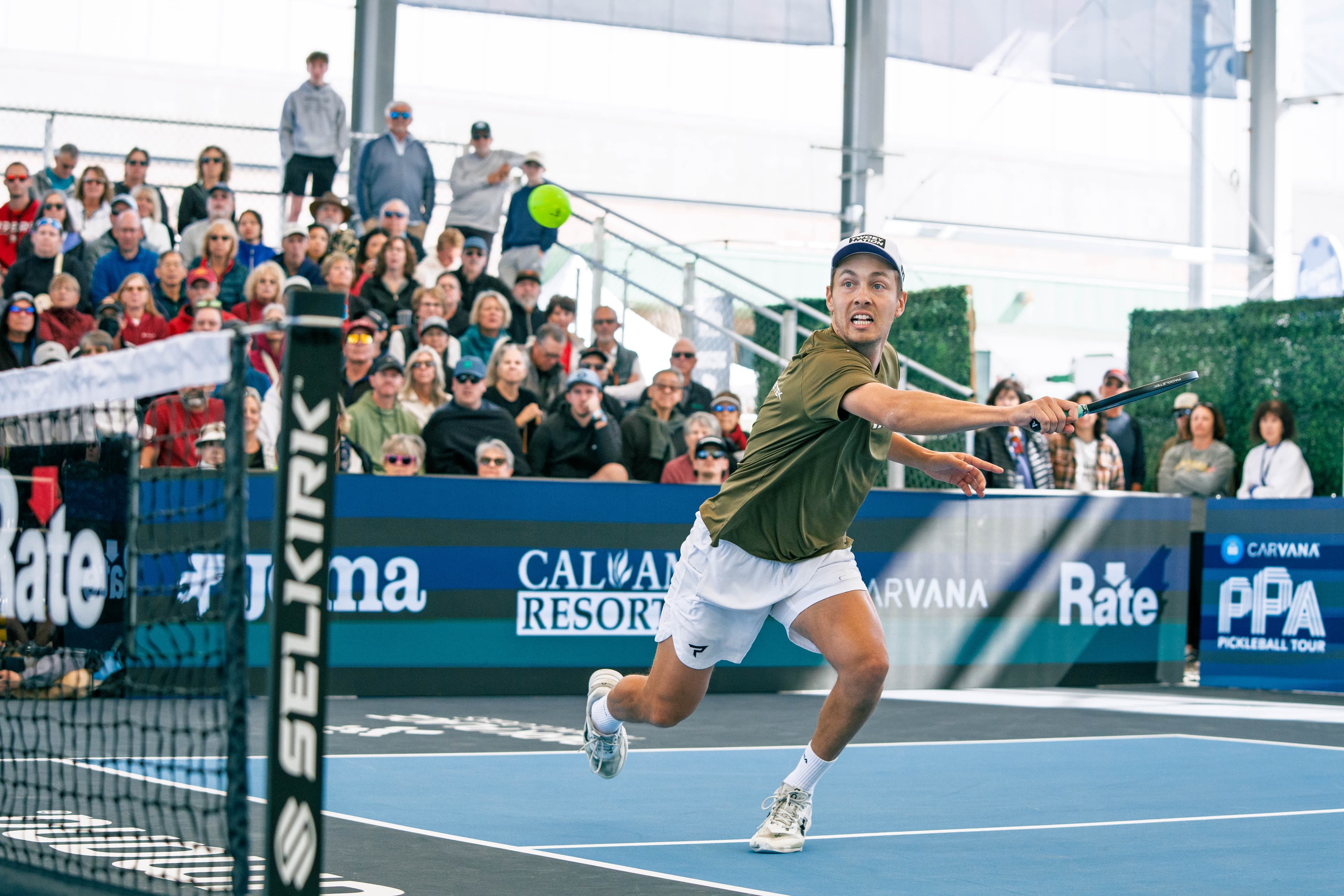 Connor Garnett stretching for a backhand during a PPA Tour singles match, full grandstand behind the court